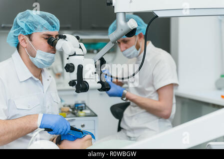 Arzt Mikroskop. Zahnarzt ist die Behandlung von Patienten in der modernen zahnmedizinischen Büro. Die Bedienung erfolgt mittels Fangdamms durchgeführt. Client wird eingefügt und restauriert, Zähne, Zahnersatz. Stockfoto