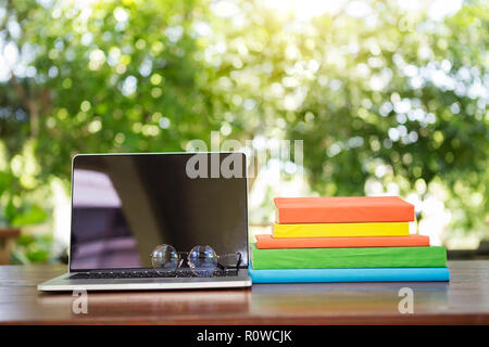 Geöffnet Laptop mit Brille und Bücher auf Holz Tisch mit unscharfer Natur Hintergrund gestapelt. Business oder Bildung.