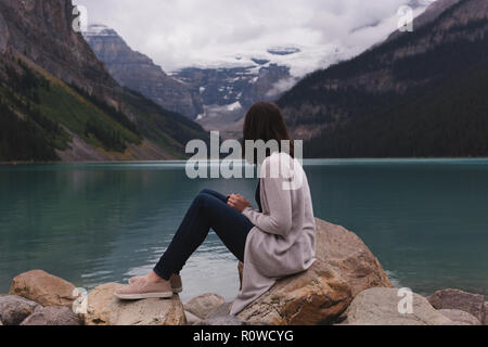 Frau sitzt auf Felsen in der Nähe von Lakeside Stockfoto