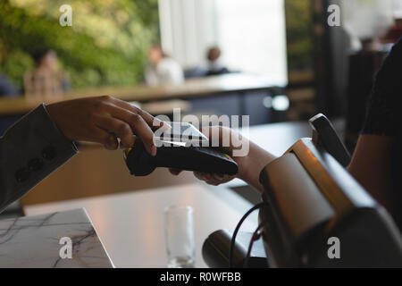 Frau Bezahlen mit Handy über NFC-Technologie bei Cash Counter Stockfoto