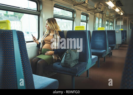 Schwangere Frau mit Handy während in Zug Stockfoto