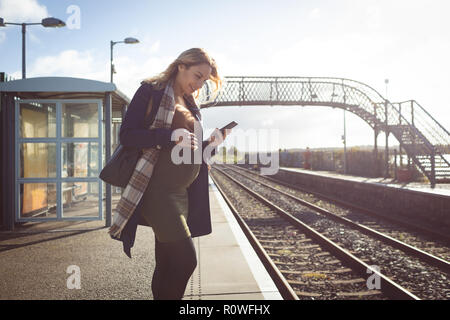 Schwangere Frau mit Handy auf der Plattform Stockfoto