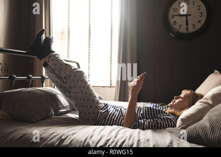 Frau mit Handy auf dem Bett im Schlafzimmer Stockfoto