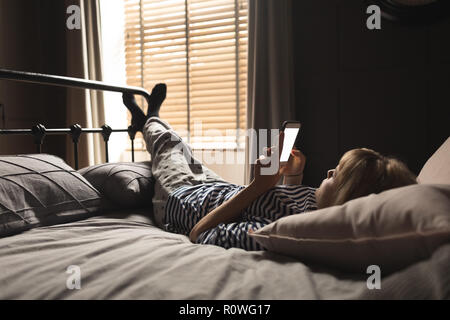 Frau mit Handy auf dem Bett im Schlafzimmer Stockfoto