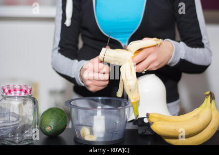 Die Frau in der Küche Schnitte Banane mit Messer in Blender. Frisches Obst für den Smoothie zu trinken auf dem Schreibtisch. Detox und gesundes Essen Konzept. Close Up, selektiver Fokus Stockfoto