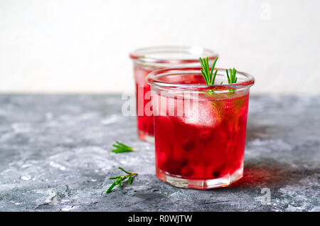 Cranberry Cocktail mit Eis und Rosmarin auf grauen Hintergrund, erfrischendes Getränk Stockfoto