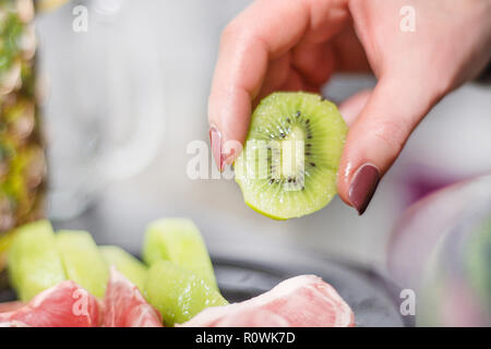 Grüne geschälte Kiwi Frucht hält Frau Hand. Salat und Obst gesund essen Konzept. Schönes Licht verschwommenen Hintergrund. Close Up, selektiver Fokus Stockfoto