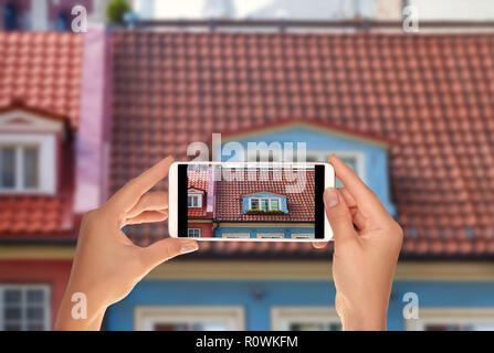 Ein Tourist ist ein Foto von Fenster mit Blumen in das Dach eines alten Hauses in der Altstadt von Riga, Lettland auf einem Mobiltelefon Stockfoto