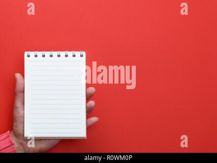 Weibliche Hand, die eine offene Notebook mit leere weiße Seiten auf einem roten Hintergrund, Kopie Raum Stockfoto