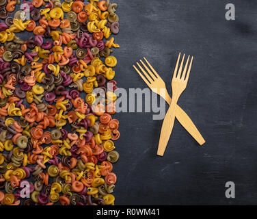 Pasta bunt Spirale von Mehl von Weizen auf einem schwarzen Hintergrund und zwei hölzerne Gabeln Stockfoto