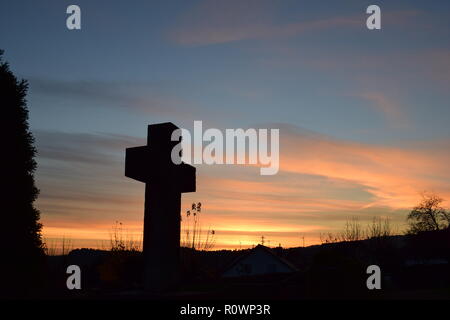 Timeline der Abenddämmerung Himmel aus gesehen hinter einem Sand Stein kreuz Skulptur während der Sonnenuntergang Sonne in der zivilen Friedhof Reimsbach, Saarland, Stockfoto