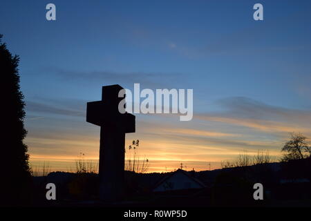 Timeline der Abenddämmerung Himmel aus gesehen hinter einem Sand Stein kreuz Skulptur während der Sonnenuntergang Sonne in der zivilen Friedhof Reimsbach, Saarland, Stockfoto