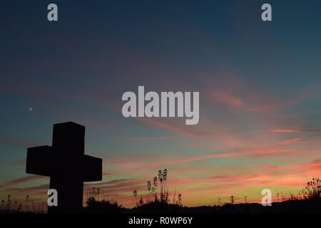 Timeline der Abenddämmerung Himmel aus gesehen hinter einem Sand Stein kreuz Skulptur während der Sonnenuntergang Sonne in der zivilen Friedhof Reimsbach, Saarland, Stockfoto