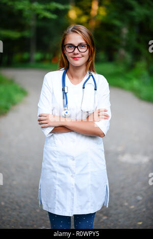 Ein junges Mädchen, die ein Arzt außerhalb steht, verschränkte die Arme auf dem Bauch. Stockfoto