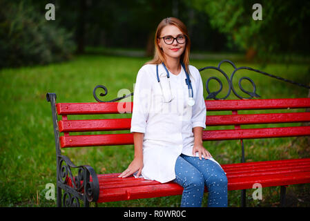 Ein junges Mädchen, die ein Arzt außerhalb steht, sitzt auf den Bänken in der Nähe des Krankenhauses Stockfoto