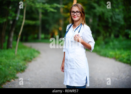 Ein junges Mädchen, das ein Arzt außerhalb steht, sie ihre Arme auf der Brust gekreuzt hat. Stockfoto