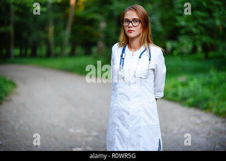 Ein junges Mädchen, das ein Arzt außerhalb steht, sie ihre Arme auf der Brust gekreuzt hat. Stockfoto