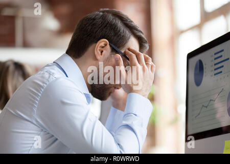 Männliche Mitarbeiter sitzen in Büro leiden unter starken Kopfschmerzen. Stockfoto