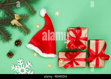 Weihnachtsdekoration. Santa's Hut, Geschenkboxen, Tannenbaum Zweige mit Zapfen und dekorative Schneeflocken auf grünem Hintergrund. Ansicht von oben. Weihnachten greetin Stockfoto