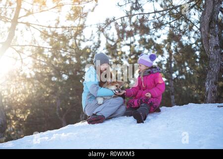 Happy Family - lächelnde Mutter und Tochter mit kleinen niedlichen Corgi flauschigen Welpen im Winter Tag Stockfoto