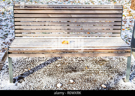 Holzbank mit gefallenen Blätter mit dem ersten Schnee im städtischen Garten im frostigen Herbst Tag abgedeckt Stockfoto