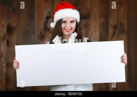 Frau mit Banner anmelden peeking über die Kante der Kopie leer Leer Billboard mit Platz für Text. Mädchen in der Weihnachtsmann hat sich lustig. Weihnachten Anzeige Stockfoto