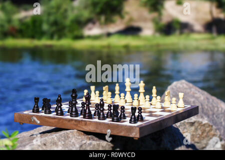Schachbrett mit Schachfiguren auf Rock mit River embankment Hintergrund. Selektiver Fokus an Bord. Im freien Spiel Schach im Sommer Stockfoto
