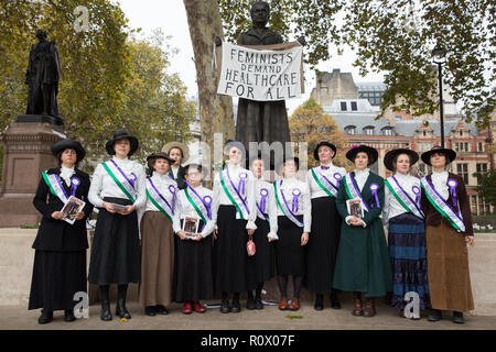 London, Großbritannien. 6. November 2018. Feministische Aktivistinnen gekleidet als Suffragetten die Millicent Fawcett statue Plakette Gesundheitsversorgung für alle zu fordern. Stockfoto