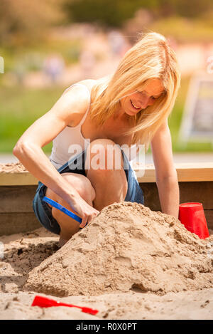 Ein hübsches, sportlich Mutter in Ihrem 40 Knuddel spielen mit ihrer Tochter im Park, das Spielen mit Sand Burgen Trentham Gardens, Stoke-on-Trent Stockfoto