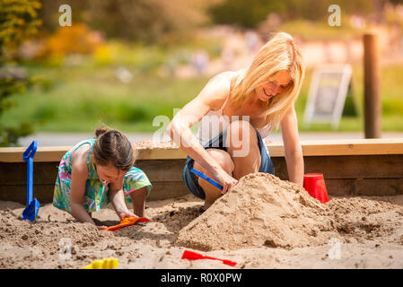 Ein hübsches, sportlich Mutter in Ihrem 40 Knuddel spielen mit ihrer Tochter im Park, das Spielen mit Sand Burgen Trentham Gardens, Stoke-on-Trent Stockfoto