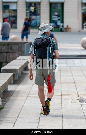 Ein Mann geht auf der Straße mit einem Rucksack. Tragen Badehose in den Rucksack befestigt. Ansicht von hinten. Stockfoto