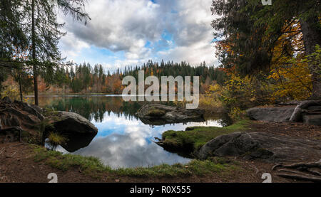 Herbst Farbe Wald und Blattwerk Landschaft umgeben einen idyllischen Bergsee in den Alpen der Schweiz, an einem späten Herbsttag mit Reflexionen im ... Stockfoto