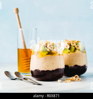 Vegan layered Bananen Dessert grüner Buchweizen, Chia Samen und Quinoa mit Blaubeer-marmelade in ein Glas mit frischem Obst, Nüssen und Honig. Gesunde mornin Stockfoto