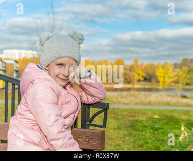 Mellow Herbst. Portrait der netten kleinen Mädchen auf einer Bank. Kopieren Sie Platz für Text. Stockfoto