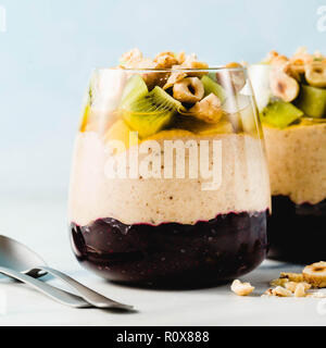 Vegan layered Bananen Dessert grüner Buchweizen, Chia Samen und Quinoa mit Blaubeer-marmelade in ein Glas mit frischem Obst, Nüssen und Honig. Gesunde mornin Stockfoto