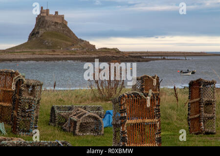 Ein Blick auf Lindisfarne Castle auf einem sonnigen und bewölkten Tag. Im Vordergrund sind Hummer Töpfe und andere Fanggeräte. Stockfoto