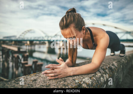 Young Sport Frau tun plank Übung auf der Wand während outdoor Cross Training durch den Fluss fokussiert. Stockfoto