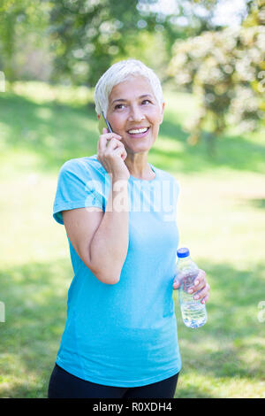 Portrait der älteren Frau in Sportbekleidung mit smart phone Outdoor Stockfoto