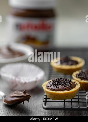 Nutella Törtchen mit Schokolade besprüht, auf einer Unterlage Rack mit Nutella im Hintergrund Stockfoto