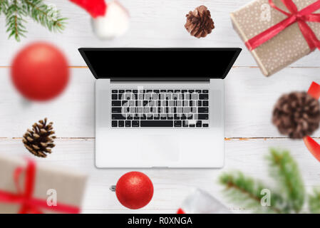 Weihnachten Geschenke und Dekorationen aus dem Laptop. Ein leerer Bildschirm am Gerät für das Mockup, website design Promotion. Blick von oben auf einen hölzernen Stockfoto