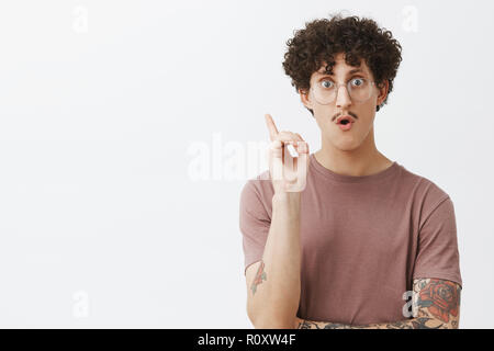 Kreative ad intelligenter junger Mann mit Schnurrbart lockige dunkle Haare und tätowiert Arm heben Zeigefinger in Eureka Geste nach Luft schnappend, tolle Idee oder Erfindung genius Plan hinzufügen Vorschlag Stockfoto