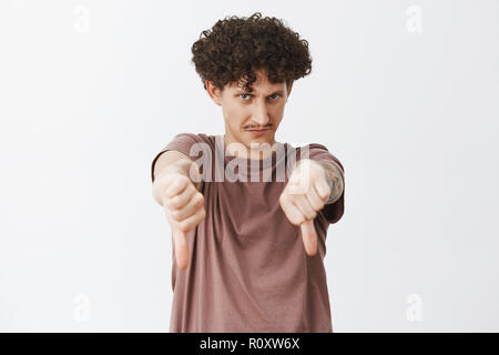 Lustige unzufrieden und unbeeindruckt jüdischen Mann mit lockigem Haar und Bart aus unter Stirn mit Mad Look mit Daumen nach unten in Abneigung Geste die negativen Feedback oder Antwort Stockfoto