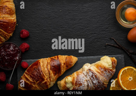 Croissants und Vanillepudding croissant umgeben mit Himbeeren, Himbeer Marmelade, Eier, Orangenscheiben und Vanilleschoten über Kopf geschossen Stockfoto