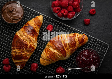 Croissants umgeben mit Himbeeren, Himbeer Marmelade und Nutella über Kopf geschossen Stockfoto