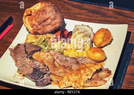 Sonntagsbraten Rind- und Schweinefleisch Abendessen mit Braten, Kartoffeln, Bohnen, Mais, Sellerie und Yorkshire Pudding. Stockfoto