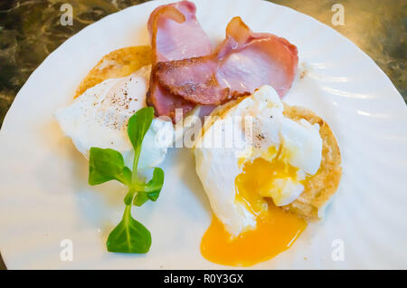 Frühstück Snack in Yorkshire ein mit zwei Scheiben Speck und zwei Weichen pochierte Eier mit einem Schnitt öffnen gerösteten muffin Stockfoto