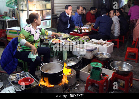 Bevormunden Gruppe Männer einen Bürgersteig Essen Einrichtung während der Inhaber Köche über offener Flamme in Hanoi, Vietnam Stockfoto