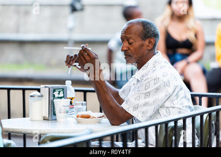 New Orleans, USA - 22. April 2018: Mann am Tisch an der berühmten kultigen Cafe Du Monde Shop, Restaurant Essen beignet Puderzucker Donuts, Kaffee, Stockfoto