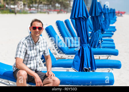 Junger Mann Mode tausendjährigen in rot Sonnenbrille am Strand während der sonnigen Tag in Miami, Florida, Blau liegen Stockfoto