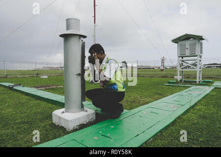 Ein Meteorologe inspiziert einen meteorologischen Regenmesser, um den Gesamtniederschlag am Flughafen Ngurah Rai zu messen. Stockfoto